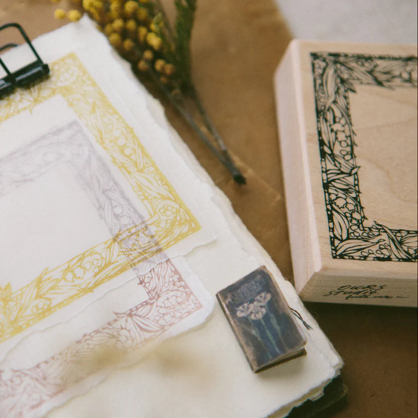 Muguet Frame Rubber Stamp block resting on paper printed with its delicate floral designs