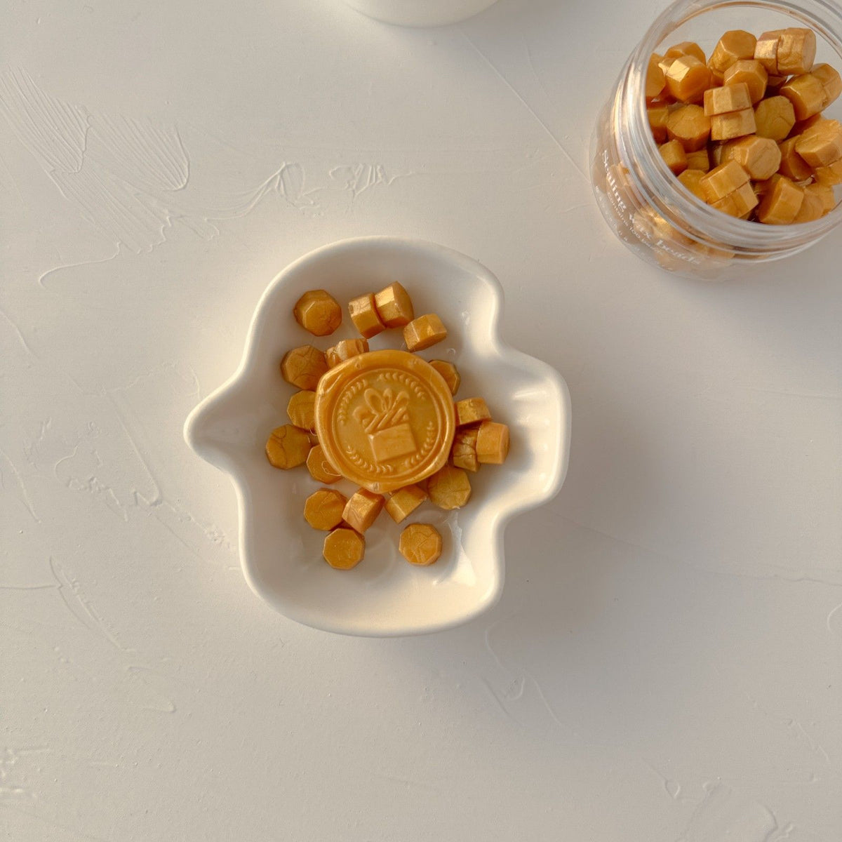 Mustard Orange sealing wax beads arranged in a sun-shaped mold on a clean white surface, top-down view