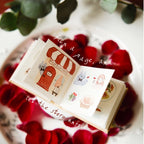 Small open book with illustrations on a bed of red petals