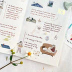 Illustrated pages with text and illustrations on a white surface with a flower.