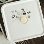 White decorative box with illustrations and a gold button on a wooden surface.