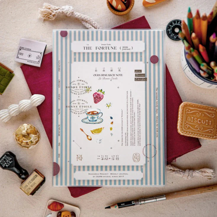 Notebook titled 'The Fortune Journal' on a desk with stationery items