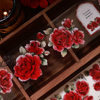 Decorative red roses on a wooden surface with a candle in the background