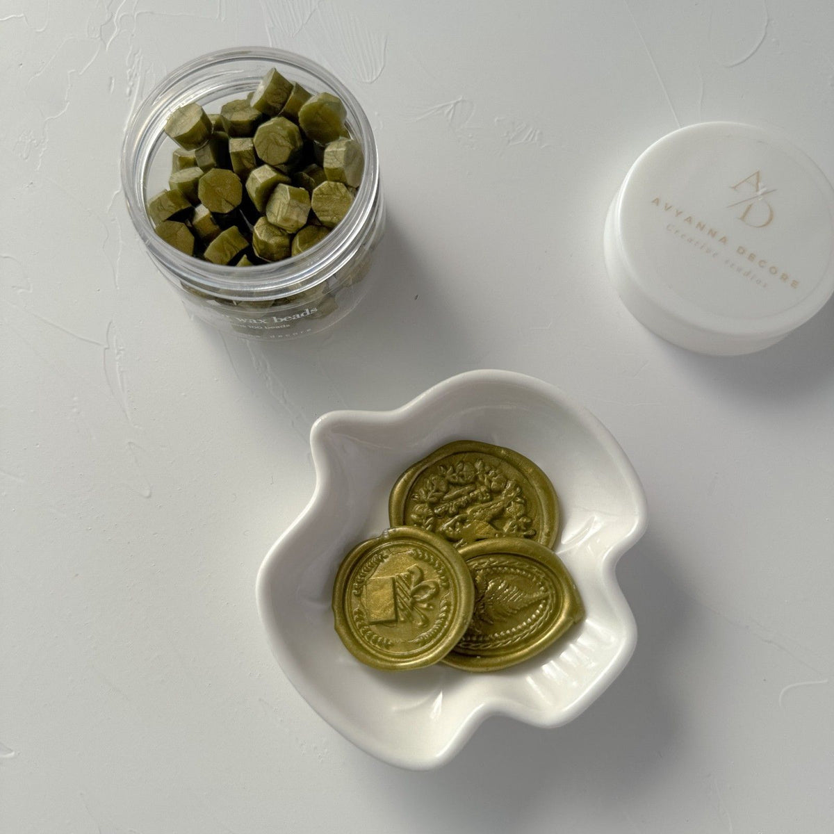 Round stamped Olive Wax Beads seals with a soft metallic sheen in a white dish on a grey background