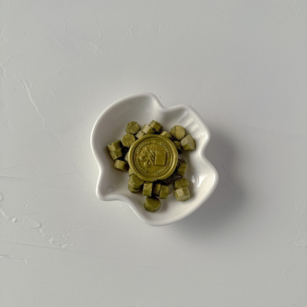Small white dish of round Olive sealing wax bead discs on a soft light grey studio backdrop, top view