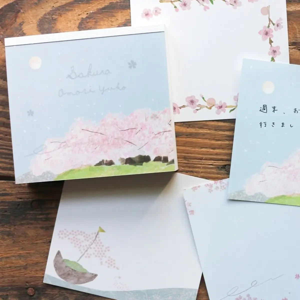 Omori Yuko Sakura Memo Pad by Cozyca with cherry blossom designs styled on a wooden surface