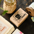 Wooden stamp with engraved design on a dark wooden surface with books and a woven container.