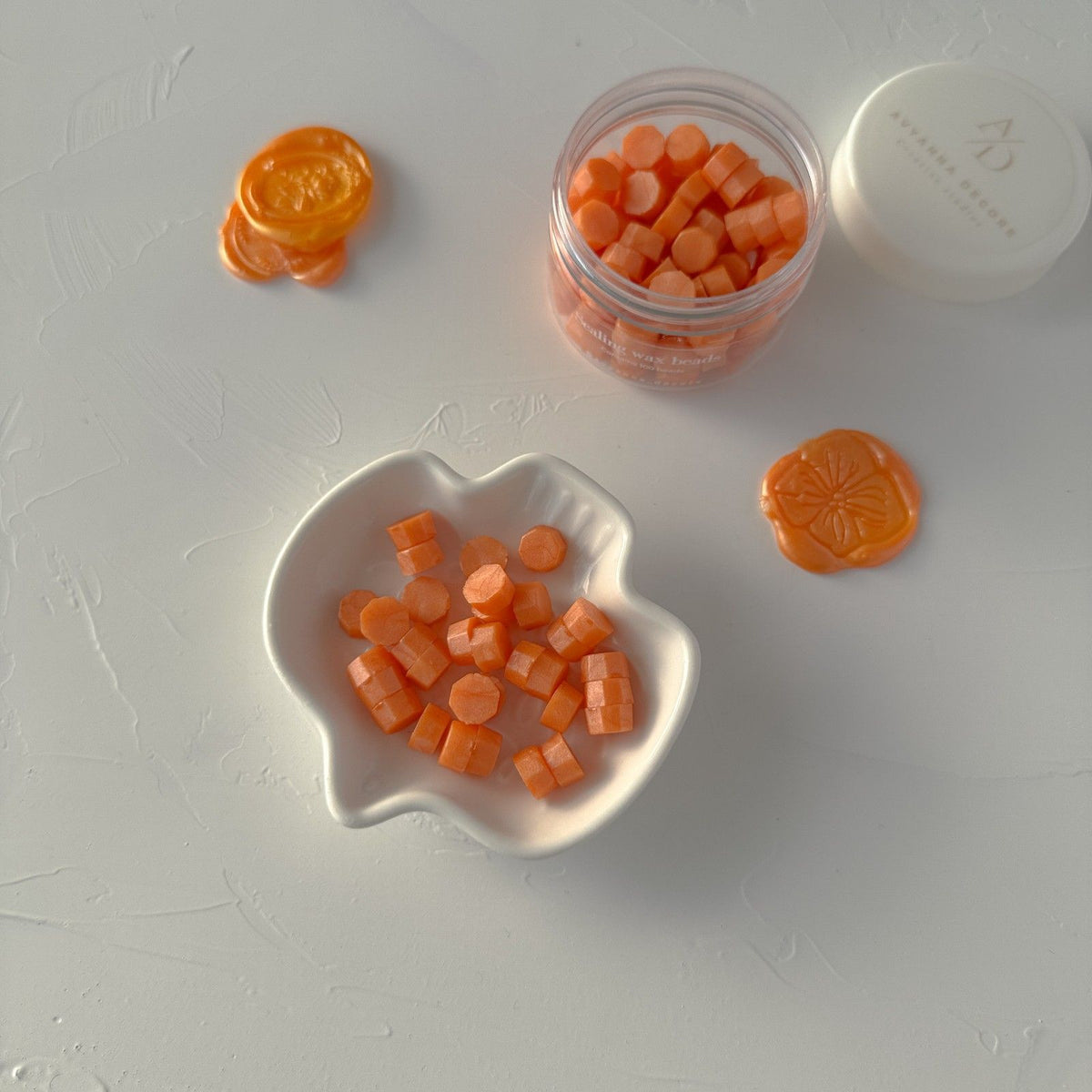 Bright Orange Wax Beads pieces in a clear container and scattered across a white surface, flat lay view