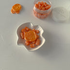 Orange candy pieces in a white leaf-shaped dish and jar on a light gray background