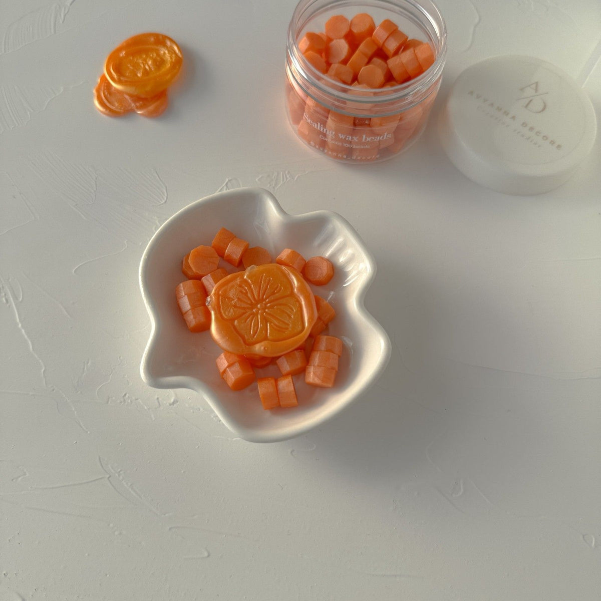 Orange Wax Beads in a white leaf-shaped dish beside the storage jar on a light grey background, top view