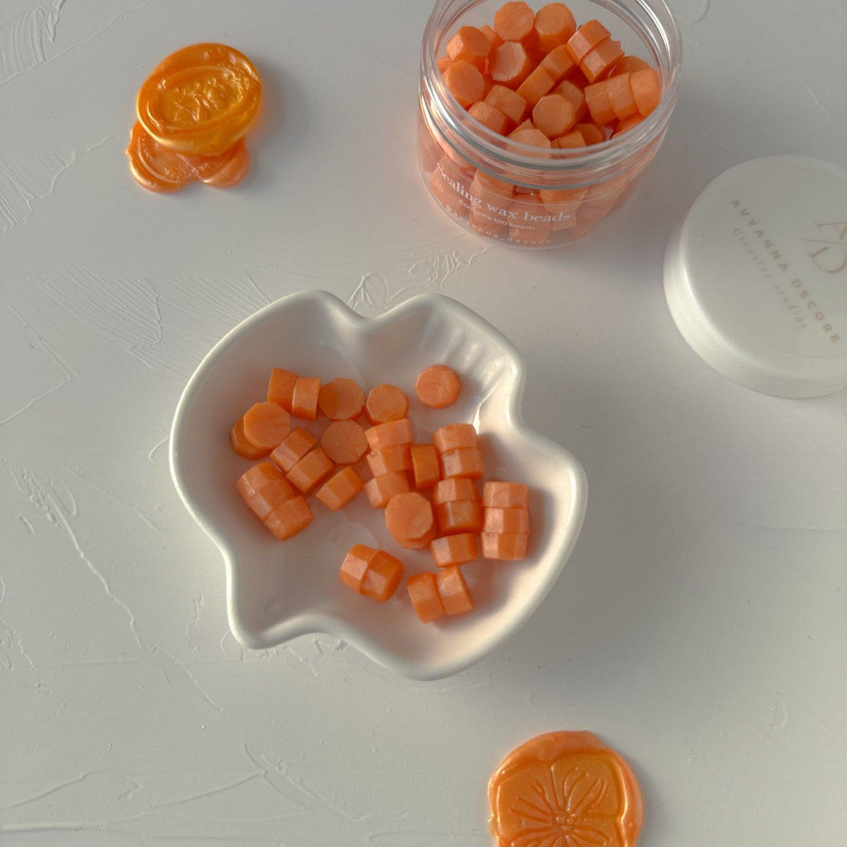 Sunny Orange sealing wax beads in a jar and spilling onto a white surface, close-up detail shot