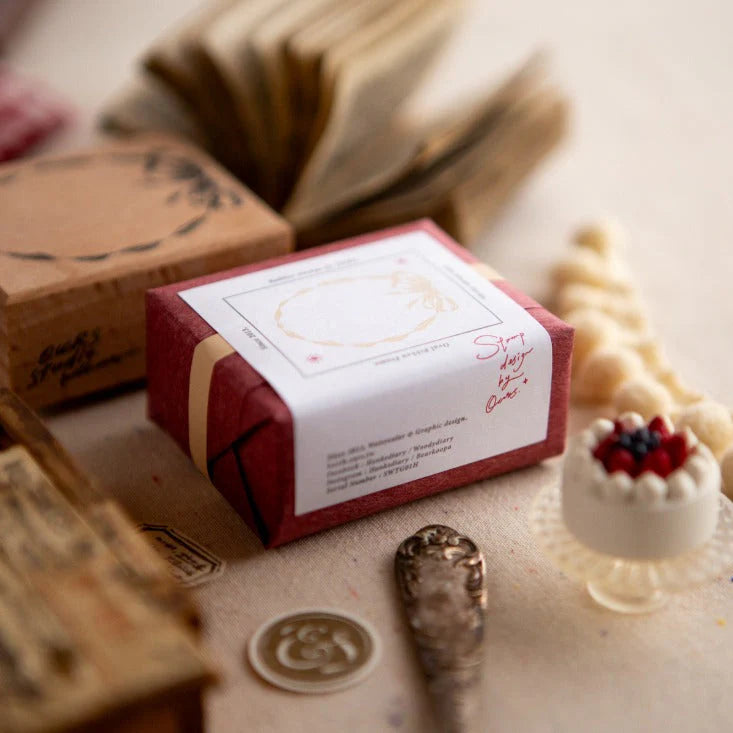 Red wrapped craft box with label styled beside the Oval Ribbon Frame Rubber Stamp and wax tools