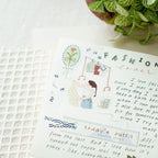 Handwritten fashion journal with illustrations and text on a textured surface with a plant in the background.
