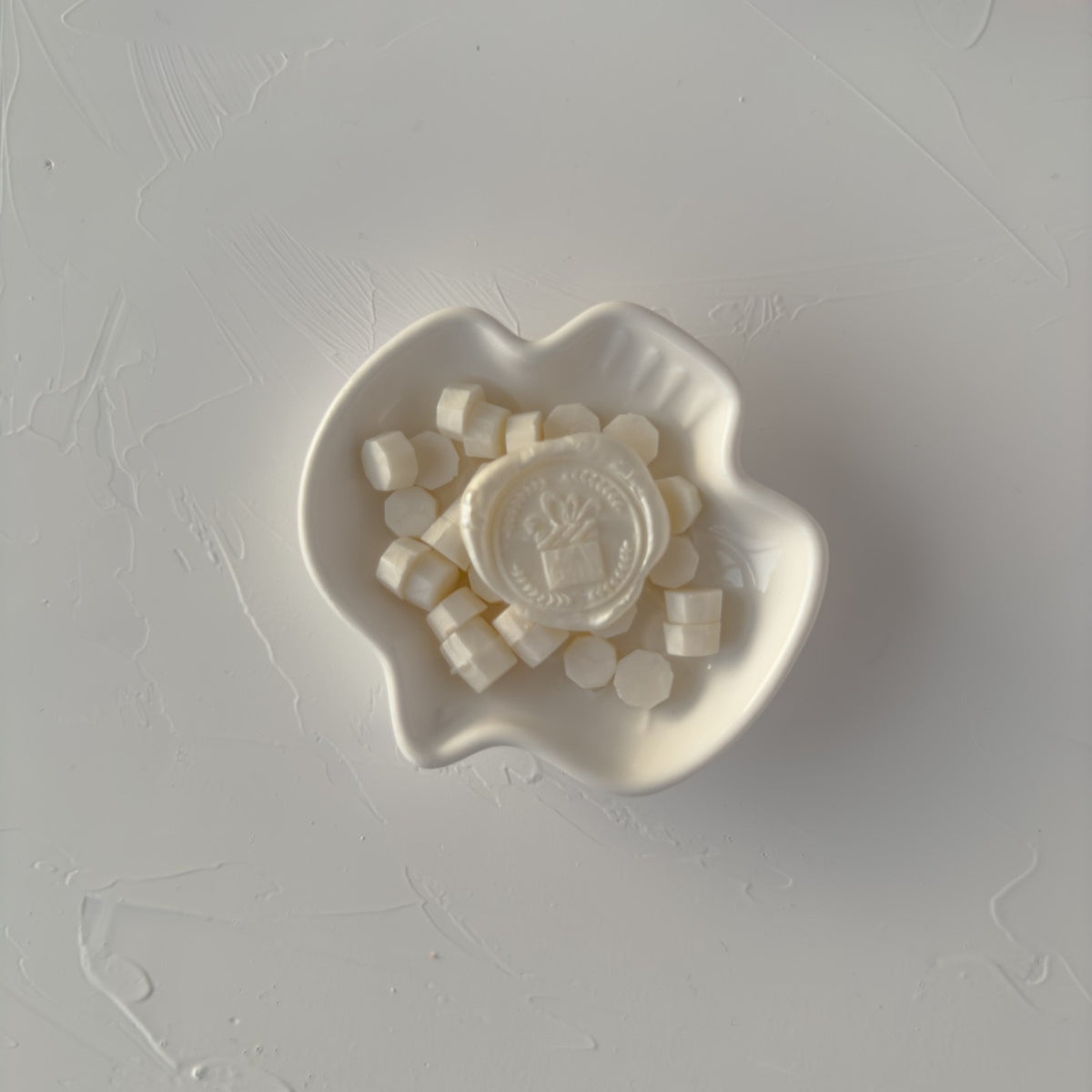 Heart-shaped dish of shimmering Pearl White sealing wax beads on a grey surface, overhead styled view