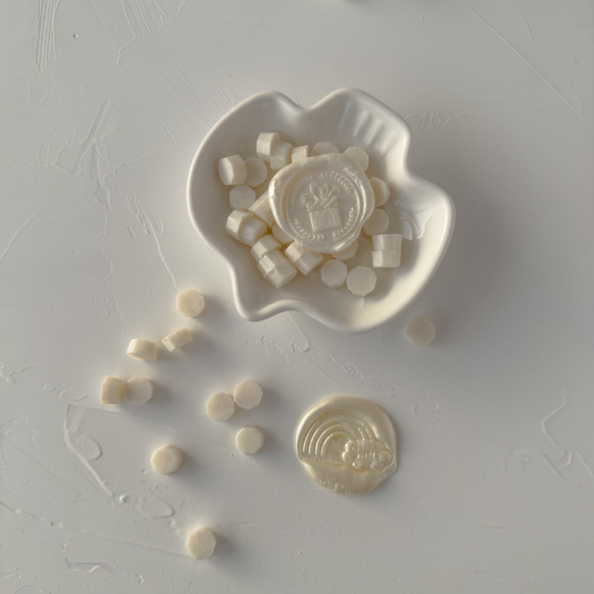 White ceramic dish of round Pearl White Wax Beads styled on a grey studio surface, close-up detail
