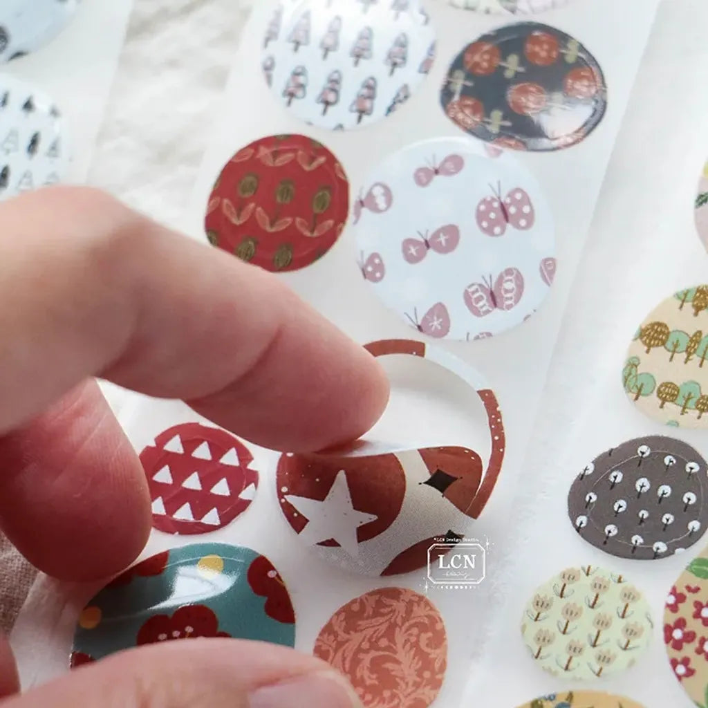 Close-up of Pebble Die-Cutting PET Tape round stickers with flowers and trees in earthy tones