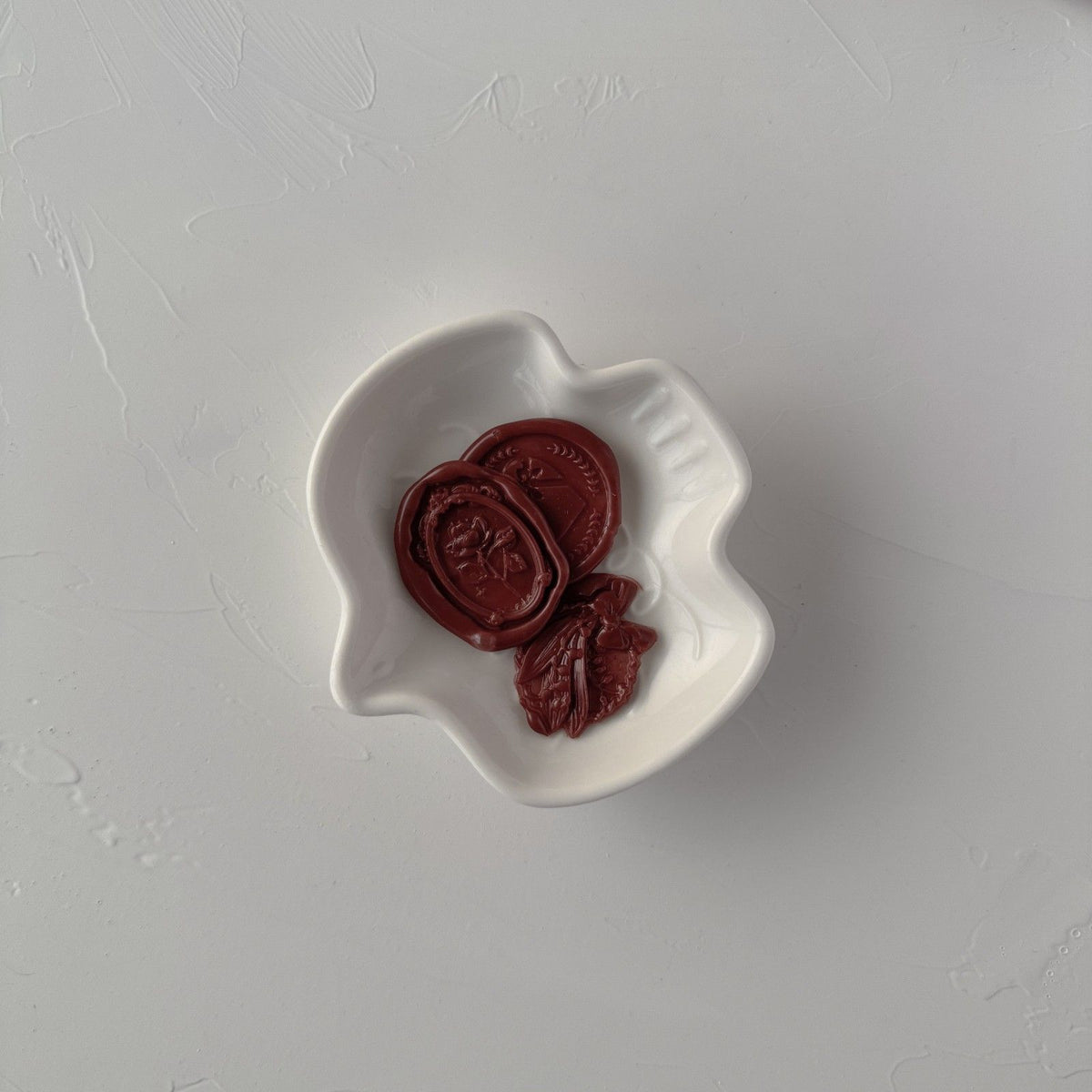 Stamped Pecan Pie wax seal impression displayed in a white dish on a light grey studio background