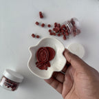 Hand holding a white heart-shaped container with red contents, surrounded by scattered red items on a light background.