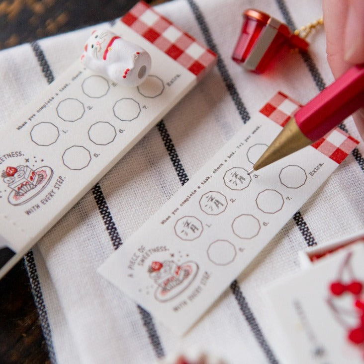 Piece of Sweetness Letterpress Memo Pad packaging with a red pen on checkered fabric