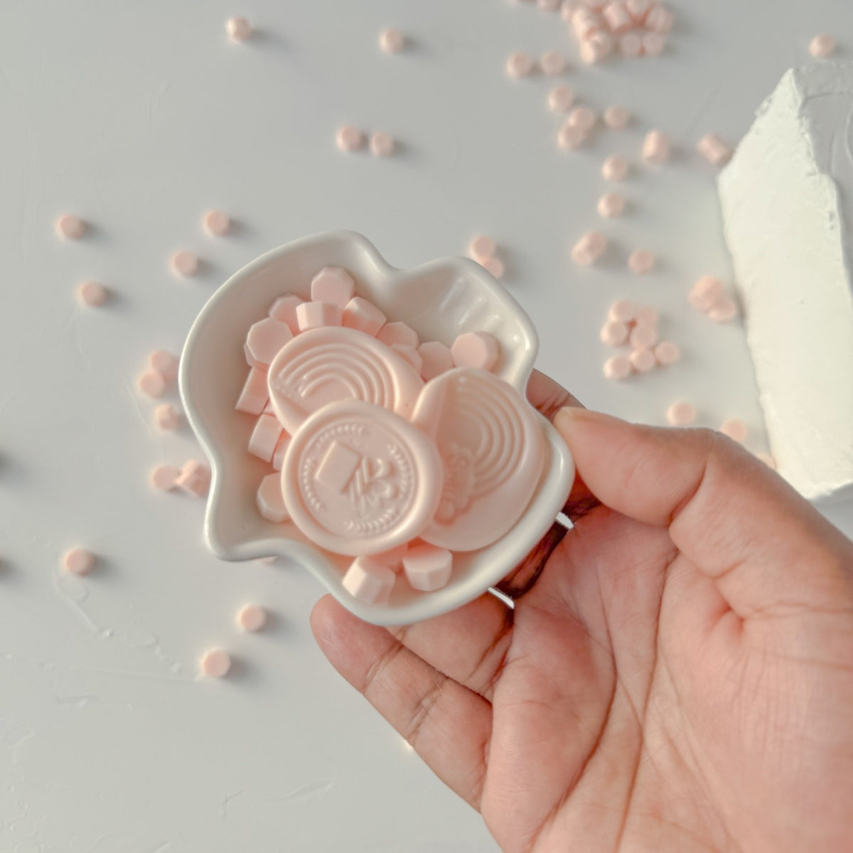 Hand holding a white container of round Pink Flamingo Wax Beads against a light grey studio backdrop