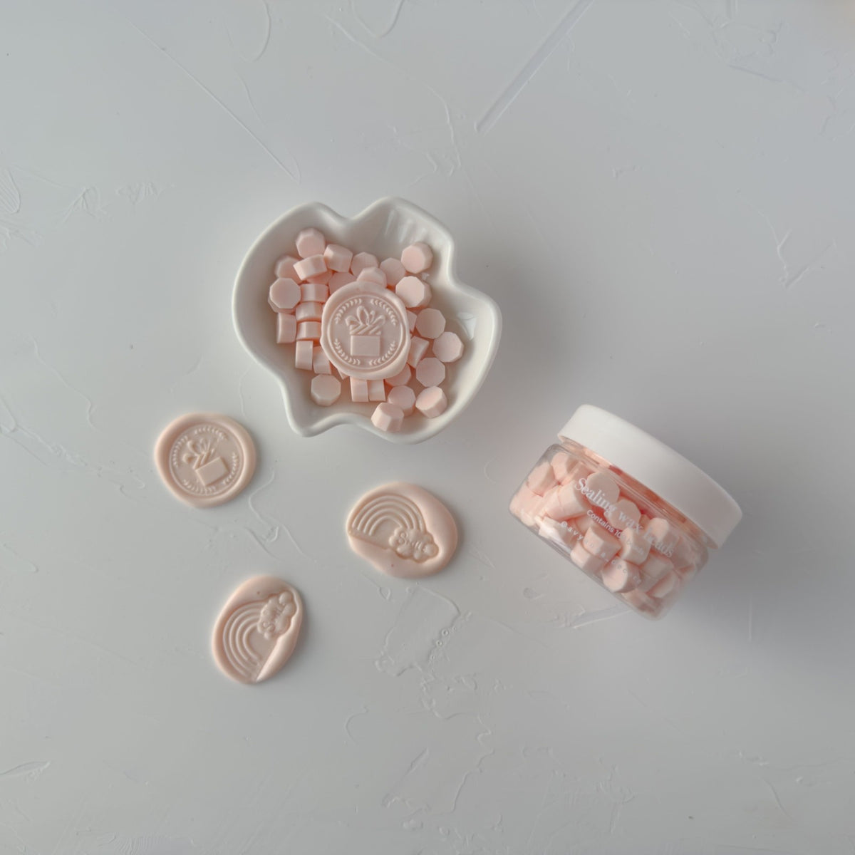 Set of stamped Pink Flamingo wax seals beside the bead container, flat lay on a light grey background