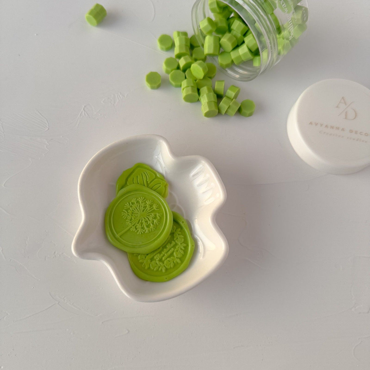 Pastel green hexagonal Pistachio sealing wax beads in a white dish on light grey