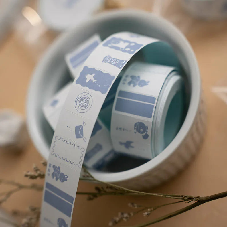 Rolls of decorative tape with cartoon designs in a white container on a wooden surface.