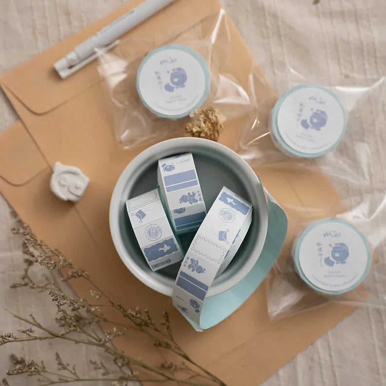 Small containers labeled with Post Label Sticker Tape designs arranged on a wooden surface