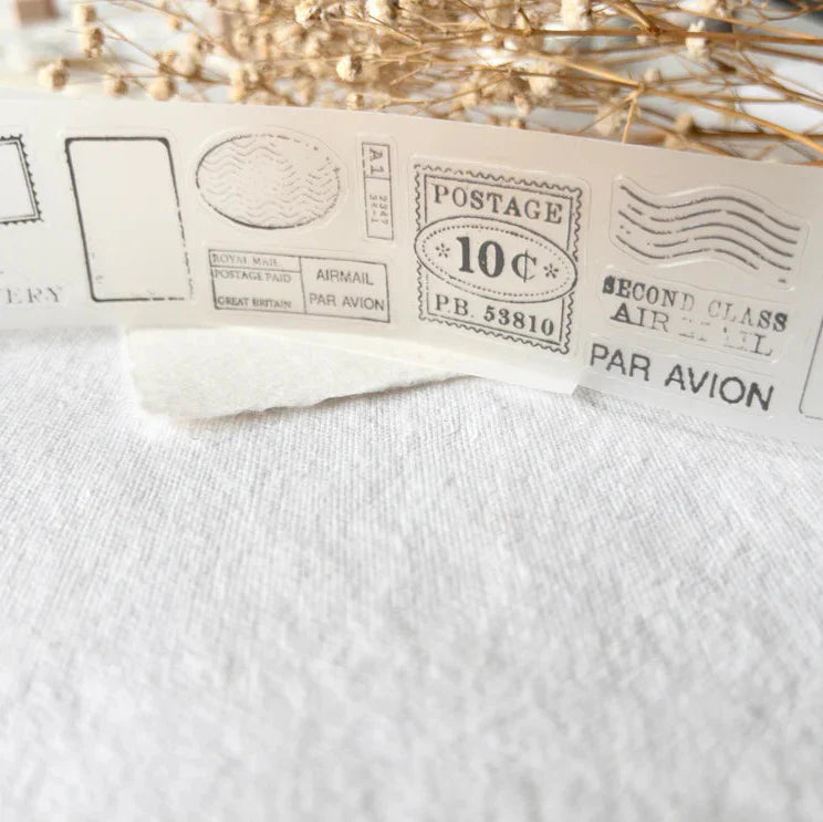 Vintage-style Posted PET Tape stamp designs displayed on white fabric with dried flowers around