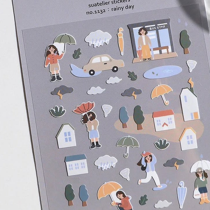 Sheet of 'rainy day' themed stickers with people, umbrellas, cars, and houses on a gray background.