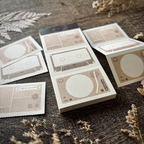 Cassette tape-themed stationery items on a wooden surface with dried plants.