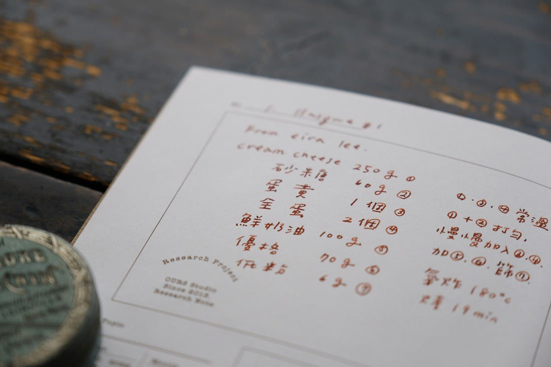 Handwritten recipe entry in the Research Notes Notebook with a coin in the foreground