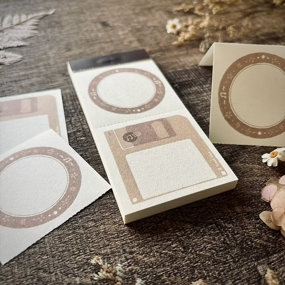 Retro Floppy Disk Memo Pad by A Great Idea with bordered sheets displayed on a wooden surface