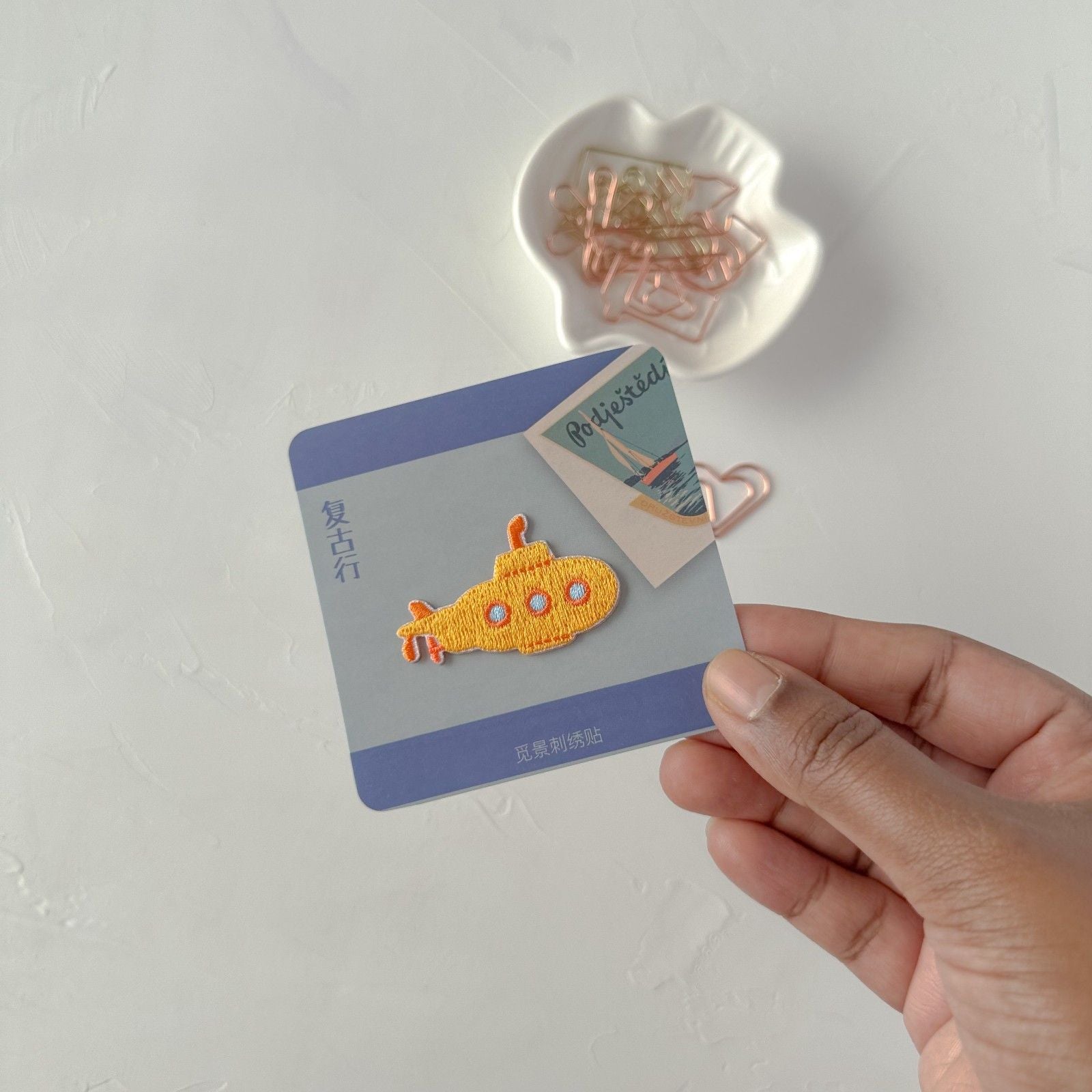 Hand holding a card with an embroidered yellow submarine design on a white background