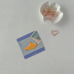 Yellow submarine card with blue border on a white surface, surrounded by paper clips.