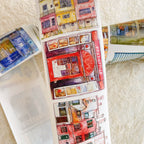 Decorative paper strip with watercolor designs of buildings and a post office on a textured surface.