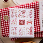 Sheet of decorative stamps with red ribbons and numbers on a red and white checkered fabric background.