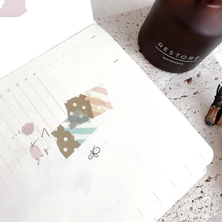 Notebook styled with Rose Calligraphy PET Tape quote stickers next to a Restore bottle, flat lay view