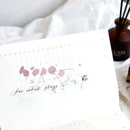 Notebook with floral design and text on a white surface with a diffuser in the background