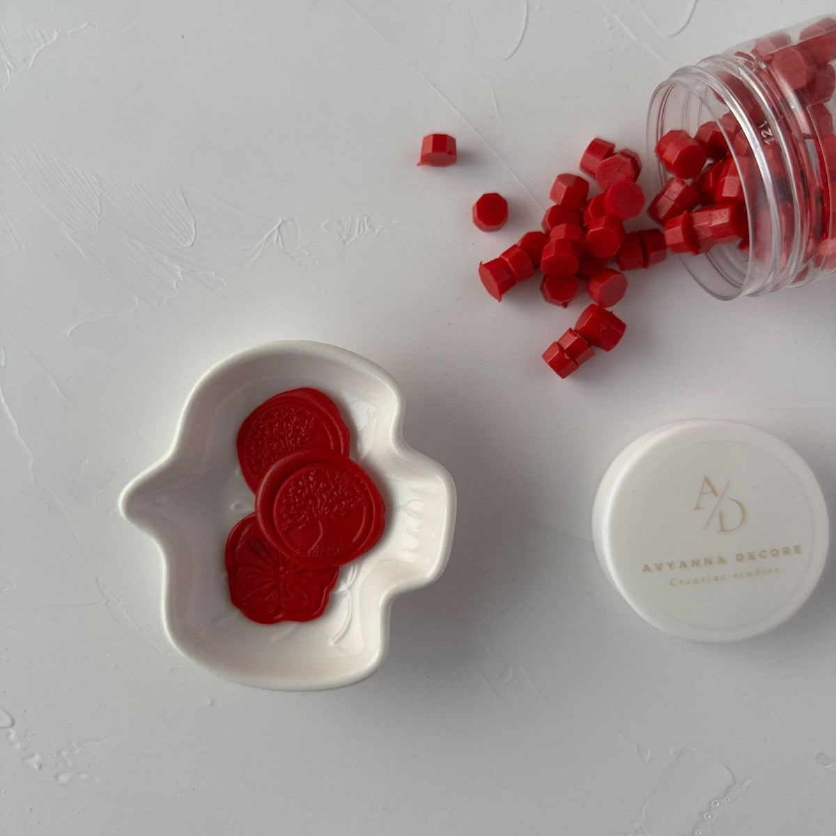Scarlet sealing wax seal resting on a mold with the container of red beads behind, on a white surface