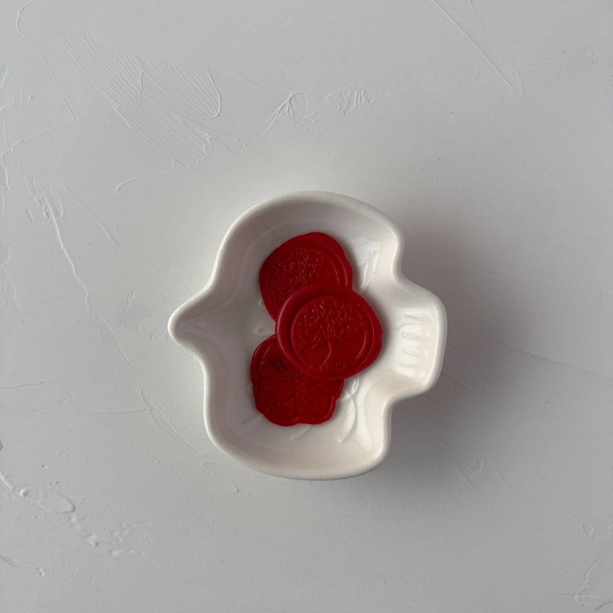 Single stamped Scarlet wax seal displayed on a small white dish against a light grey studio background