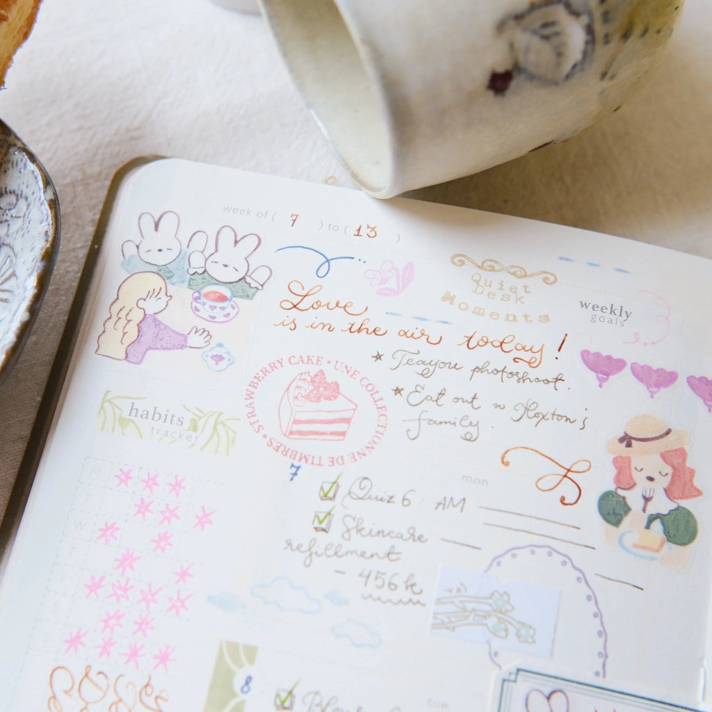 Open planner with decorative stickers and a cup on a table