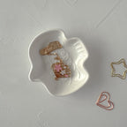 White cat-shaped dish with gold jewelry and paper clips on a light gray surface
