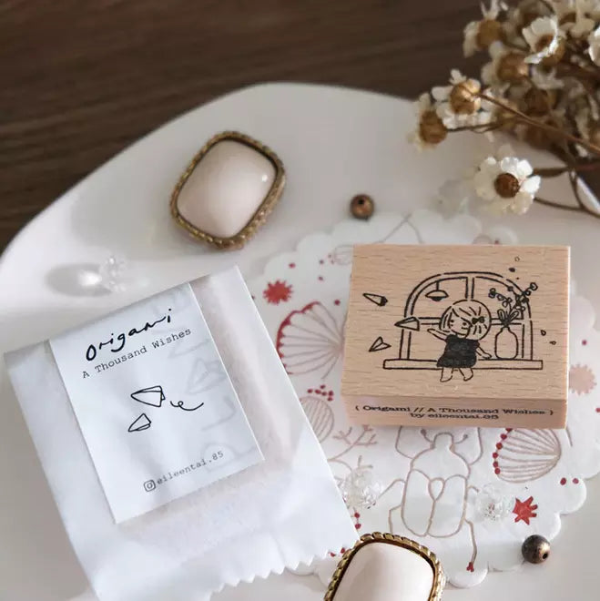 A Thousand Wishes Paper Planes stamp with its packaging on a decorative plate with flowers