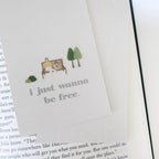 Book with a bookmark featuring a couple on a bench and trees, with text 'i just wanna be free.'