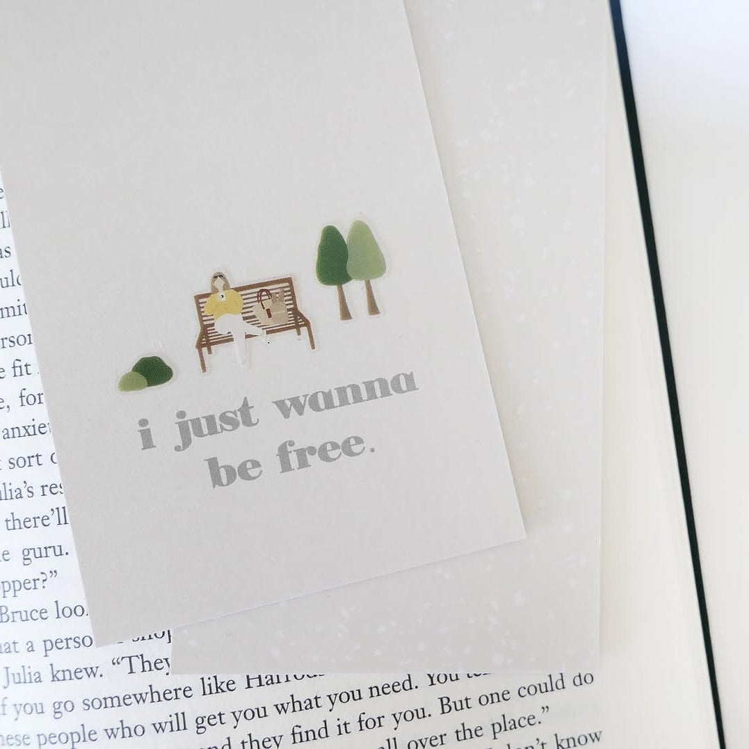Book with a bookmark showing a couple on a bench and trees, from the Slow Day Sticker Sheet