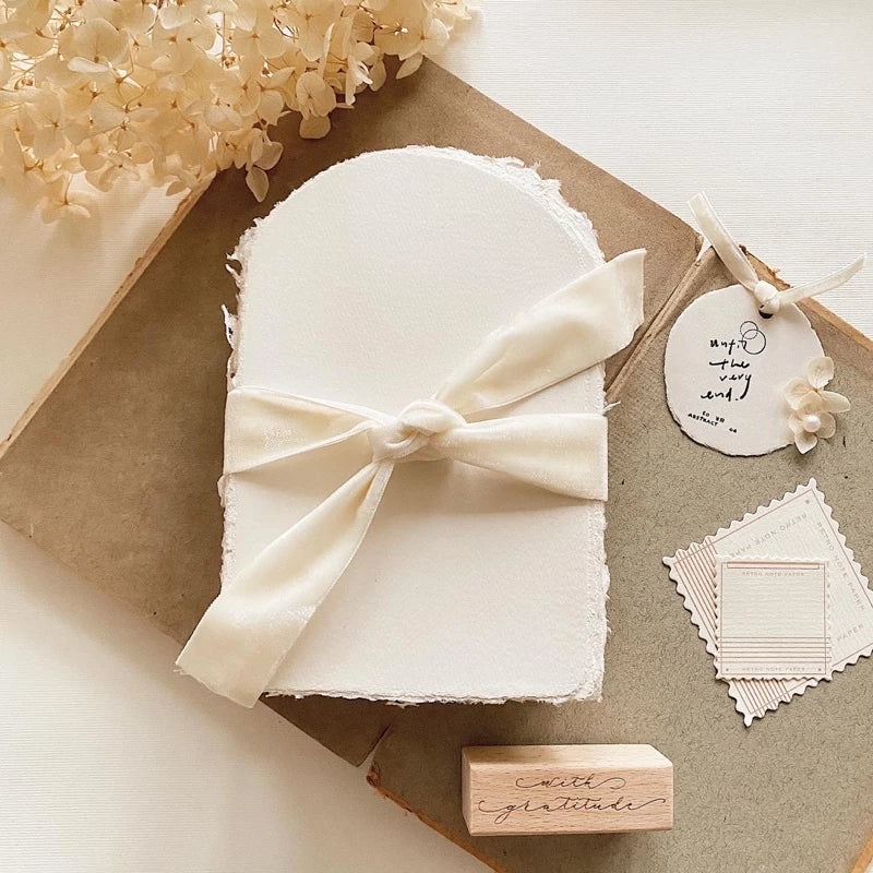 White folded paper with a bow, flowers, and a wooden stamp on a light background
