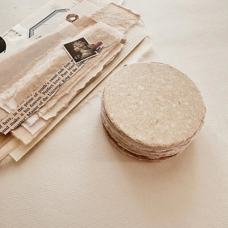 Stack of round, beige coasters on a textured surface with vintage paper and a stamp.