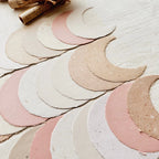 Set of crescent moon-shaped paper cutouts in various colors on a light wooden surface.