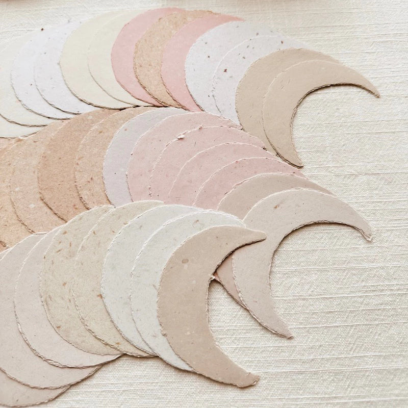 Small Moon Handmade Paper crescents in mixed pastels on a textured beige background